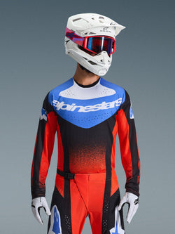 Alpinestars 2026 Techstar Knif Jersey, Motocross-Trikot, Orange, Schwarz und UCLA Blue, mit blauem Brusteinsatz, weißem Alpinestars-Logo und orange-roten Ärmeln, getragen mit weißem Helm, roter Brille und weißen Handschuhen, professionelle Offroad-Rennausrüstung