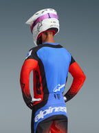 Rückansicht eines Motocross-Fahrers im 2026 Techstar Knif Jersey in Orange Black UCLA Blue, mit einem blauen Rückenteil mit lasergeschnittenen Perforationen, orangefarbenen Ärmeln und schwarzen Akzenten, kombiniert mit einer passenden Motocross-Hose und einem weißen Alpinestars-Helm.