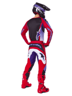 Motocross-Fahrer von hinten im Alpinestars 2025 Fluid Wurx Gear Set, lila-hellrotes Trikot mit schwarzem Rückeneinsatz, passende Motocross-Hose mit weißen und lila Akzenten, hellrote Stiefel und schwarzer Helm, professionelles Offroad-Rennoutfit
