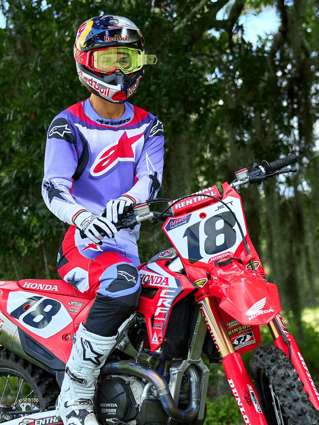 Motocross-Fahrer auf einem roten Honda CRF Dirtbike, trägt Alpinestars 2025 Fluid Wurx Trikot in Lila und Hellrot, passende lila und rote Hose, Red Bull Helm mit gelber Brille, weiße Alpinestars Stiefel und Handschuhe, professionelle MX-Ausrüstung für Offroad-Fahrten