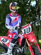 Motocross-Fahrer auf einem roten Honda CRF Dirtbike, trägt Alpinestars 2025 Fluid Wurx Trikot in Lila und Hellrot, passende lila und rote Hose, Red Bull Helm mit gelber Brille, weiße Alpinestars Stiefel und Handschuhe, professionelle MX-Ausrüstung für Offroad-Fahrten