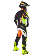 Alpinestars 2025 Fluid Wurx Ausrüstungsset, Motocross-Trikot und -Hose in Gelb, Schwarz und Orange, dargestellt in der Dreiviertel-Rückansicht, kombiniert mit passendem schwarzem Helm und leuchtend gelben Stiefeln, professionelle Offroad-Rennausrüstung.