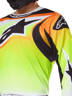 Alpinestars 2025 Fluid Wurx Trikot, Motocross-Trikot, Fluorgelb mit schwarzen und orangen Grafiken, mit einem großen schwarzen Alpinestars-Logo auf der Brust und an der Schulter, getragen von einem Fahrer mit schwarzem Helm.