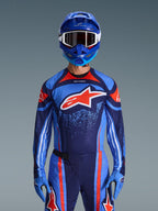 Motocross-Fahrer im Alpinestars 2026 Techstar Nomur Trikot in Dunkelblau, Orange und UCLA-Blau, passende Hose und blaue Handschuhe, blauer Helm mit weißer Schutzbrille, großes rot-weißes Alpinestars-Logo auf der Brust, abgestimmte Performance-Ausrüstung für den Offroad-Rennsport