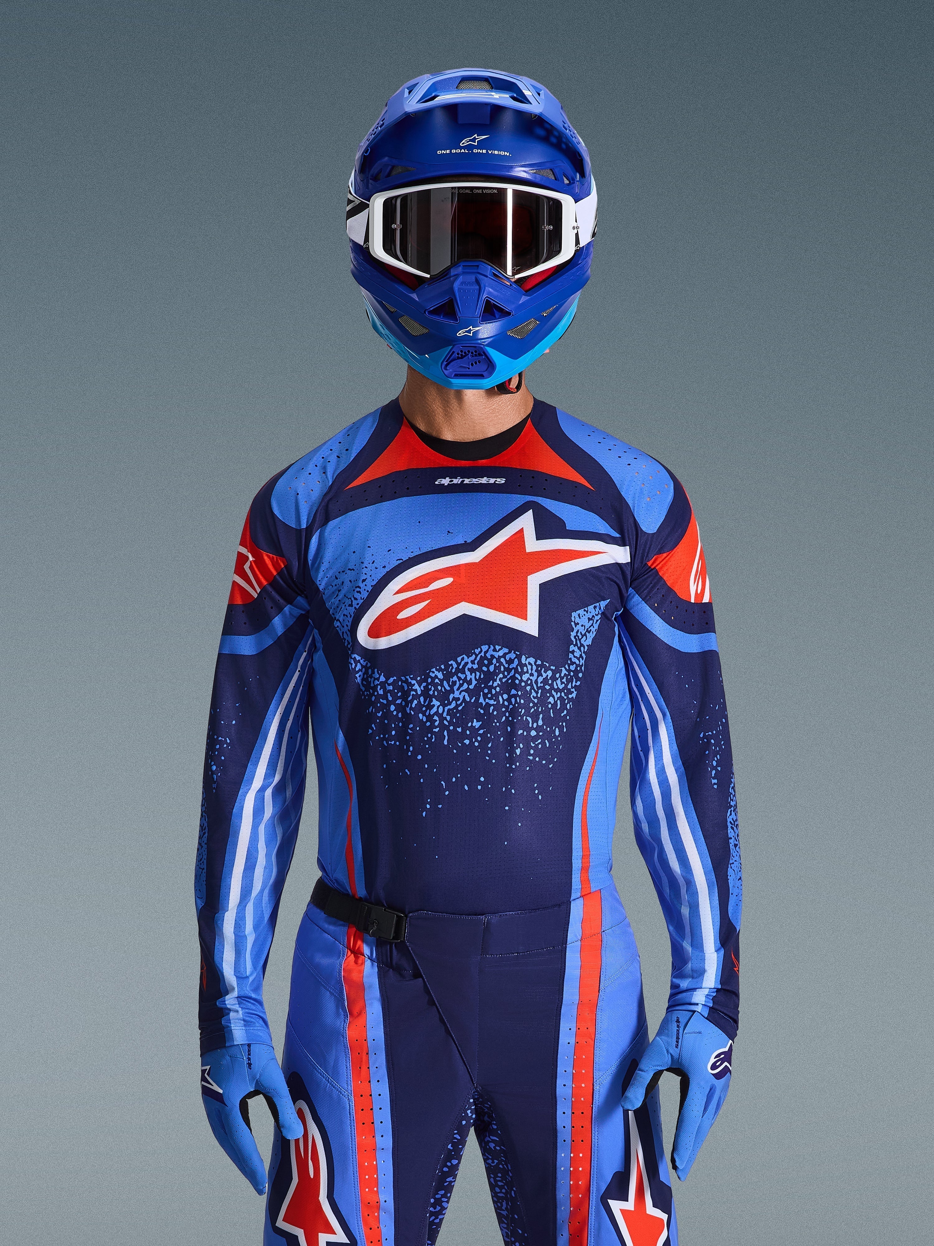 Motocross-Fahrer im Alpinestars 2026 Techstar Nomur Trikot in Dunkelblau, Orange und UCLA-Blau, passende Hose und blaue Handschuhe, blauer Helm mit weißer Schutzbrille, großes rot-weißes Alpinestars-Logo auf der Brust, abgestimmte Performance-Ausrüstung für den Offroad-Rennsport
