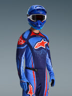 Motocross-Fahrer mit Alpinestars 2026 Techstar Nomur Trikot, Rennbekleidung in Dark Navy, Orange und UCLA Blue, mit großem orangefarbenem Astars-Logo, passendem blauem Helm und Handschuhen, sportliches Offroad-Wettbewerbs-Outfit.