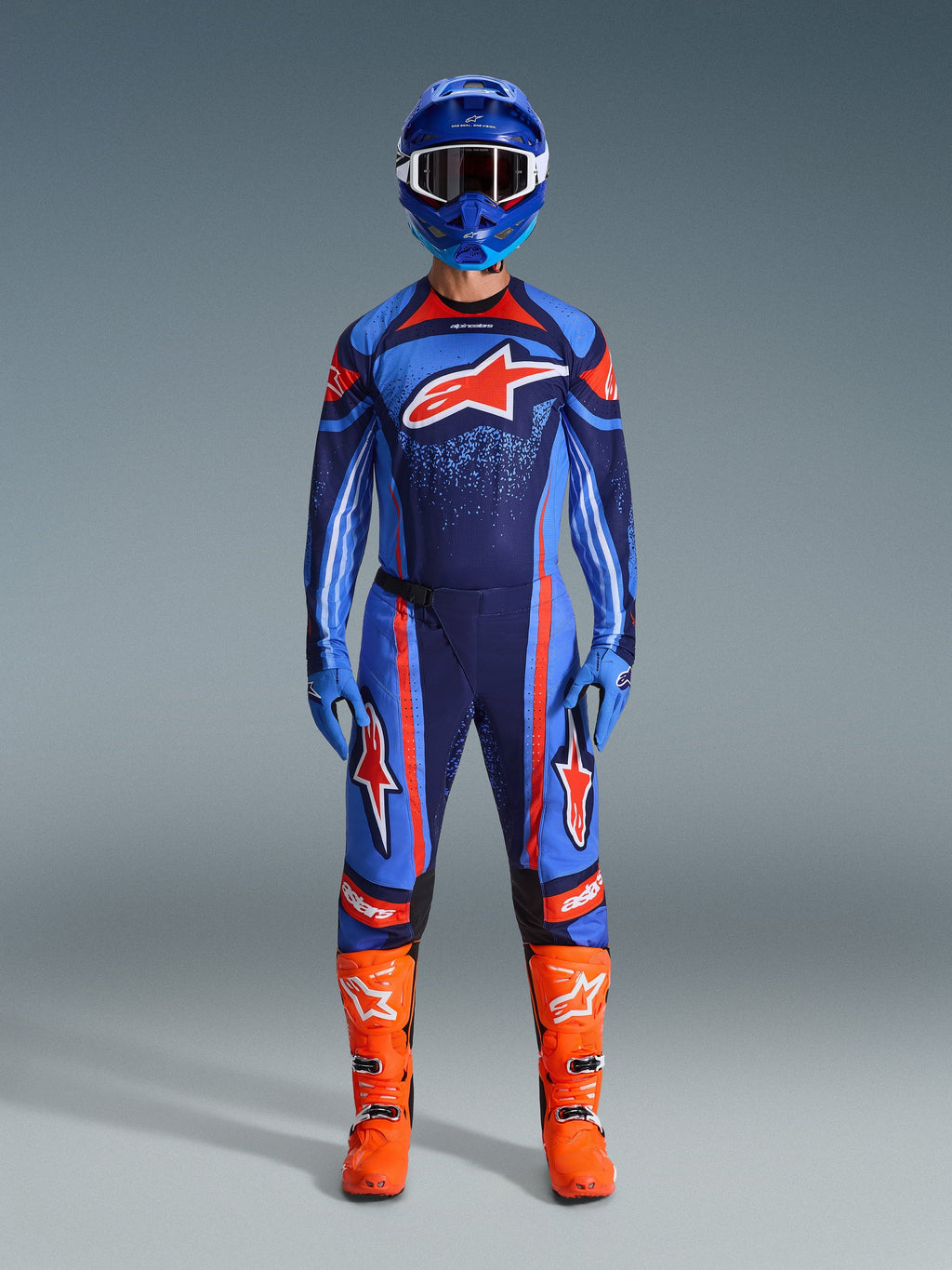 Motocross-Fahrer im Alpinestars 2026 Techstar Nomur Trikot in Dark Navy, Orange und UCLA Blue, kombiniert mit passender Motocross-Hose, blauem Helm mit Goggles und leuchtend orangefarbenen Rennstiefeln, komplett aufeinander abgestimmte Offroad-Wettkampfausrüstung