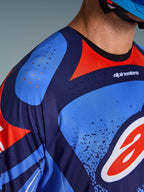 Nahaufnahme des Alpinestars 2026 Techstar Nomur Trikots, Motocross-Trikot, Dunkelblau, Orange und UCLA-Blau, mit lasergeschnittenen Belüftungsöffnungen an Schulter und Brust, technisches feuchtigkeitsableitendes Gewebe, athletisches Race-Fit-Design