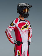 Motocross-Fahrer im Alpinestars 2026 Techstar Nomur Trikot, Rot, Weiß und Schwarz mit gelben Akzenten, kombiniert mit passender Hose, schwarzem Helm mit goldener Brille und schwarzen Handschuhen, athletische Rennpassform für professionelle Offroad-Wettkämpfe