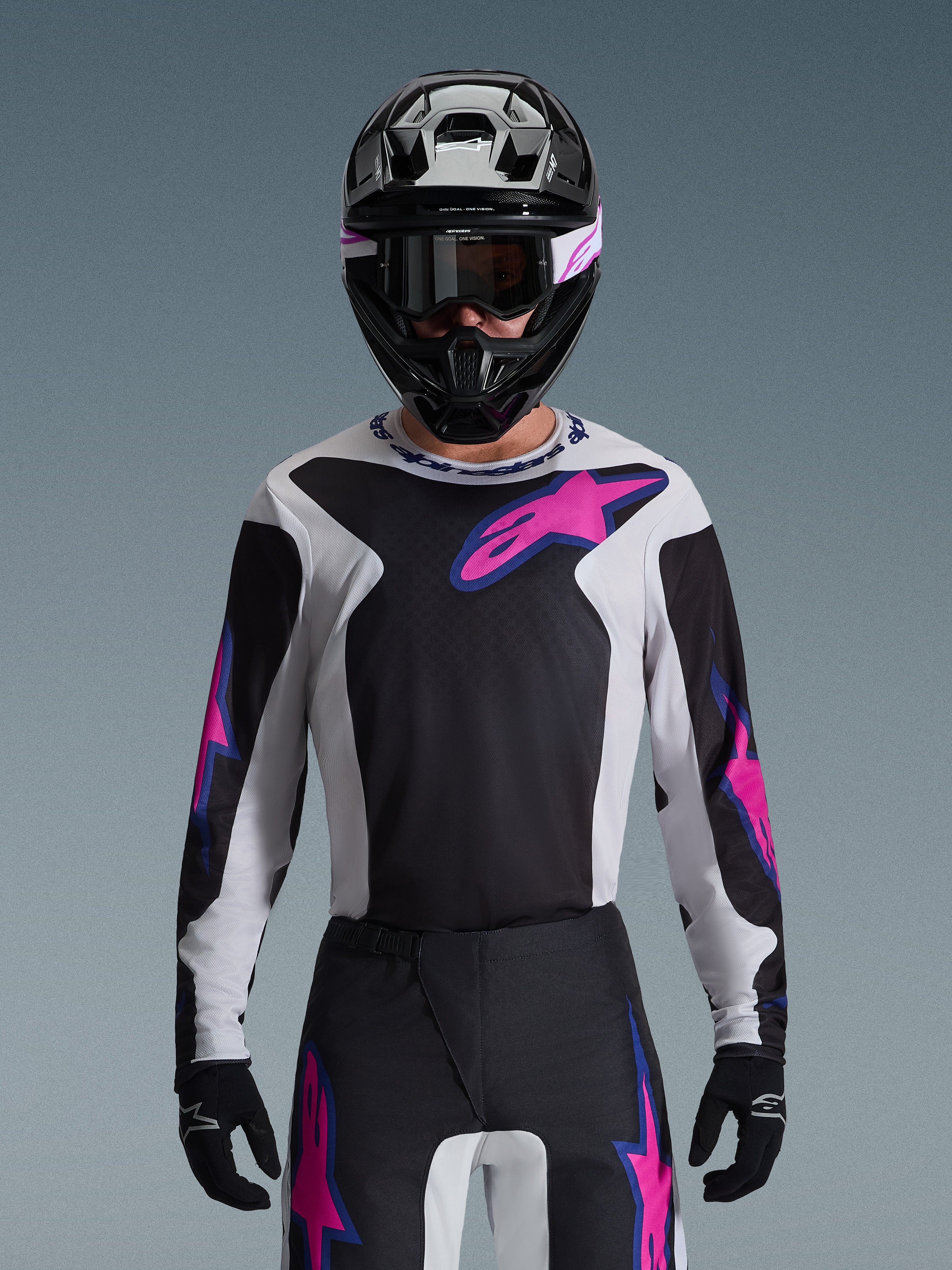 Alpinestars 2026 Fluid Grid Trikot, Motocross-Trikot, Schwarz, Hellgrau und Lila, getragen von einem Fahrer mit passender Offroad-Hose, schwarzem Helm und Schutzbrille, komplettes Performance-Rennausrüstungsset