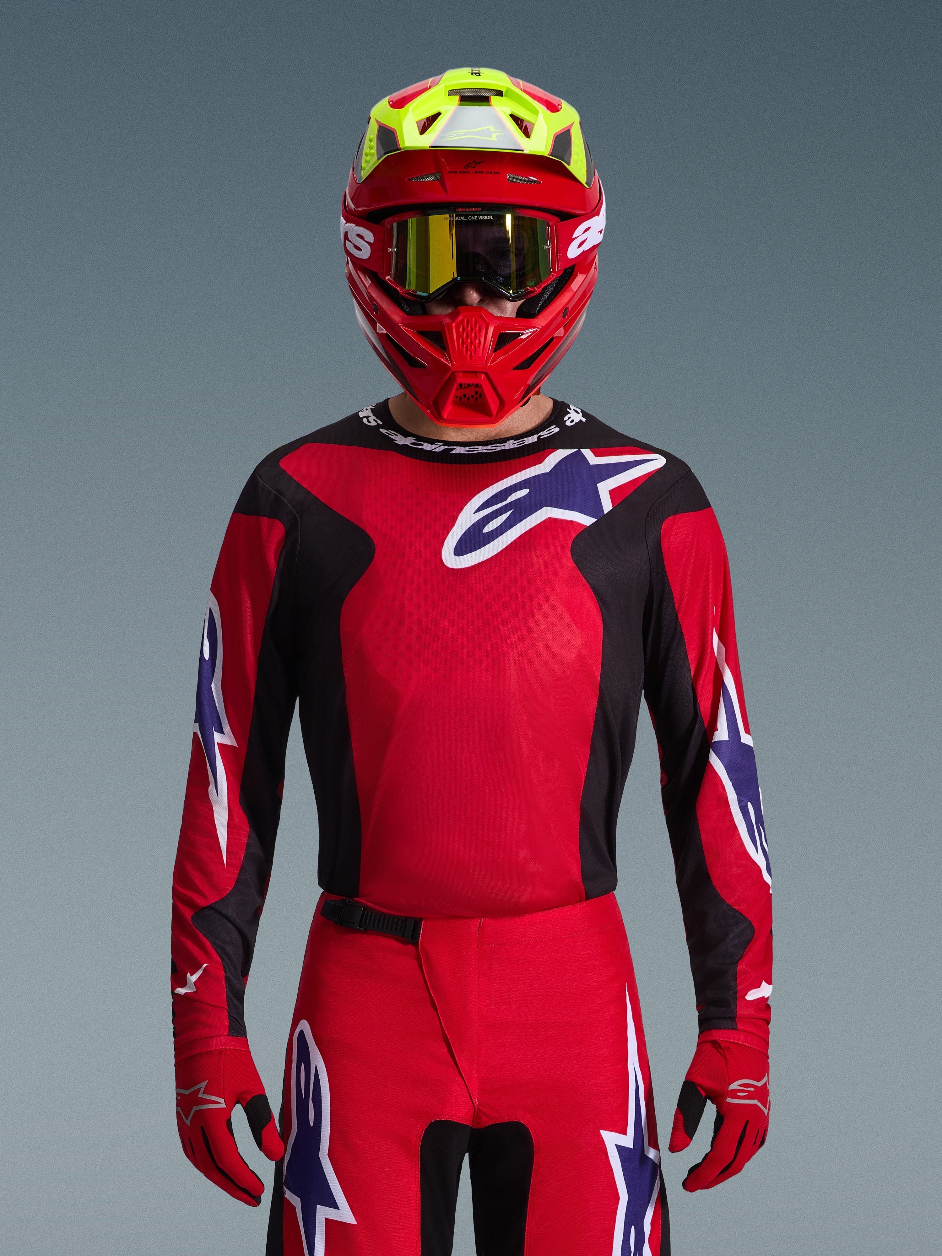 Alpinestars 2026 Fluid Grid Trikot, Motocross-Trikot, Rot, Schwarz und Lila, getragen von einem Fahrer mit einem roten und neongelben Helm und einer goldenen Goggle, mit großen Stern-Logos auf der Brust und den Ärmeln, abgestimmte Ausrüstung für den Offroad-Rennsport