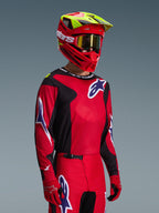 Motocross rider wearing Alpinestars 2026 Fluid Grid Gear Set, Red and Black jersey with white and blue logo accents, matching Red and Black pants, Red helmet with yellow highlights and gold goggles, coordinated off-road racing gear