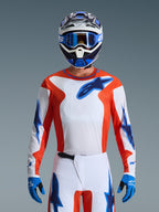 Motocross-Fahrer im 2026 Fluid Grid Jersey in Orange Ucla Blue, mit weißem Brustbereich, orangefarbenen Seitenpaneelen und blauen Alpinestars-Logos, kombiniert mit passender weiß-blauer Hose, blauen Handschuhen und einem weiß-blauen Helm für einen professionellen Offroad-Rennlook.