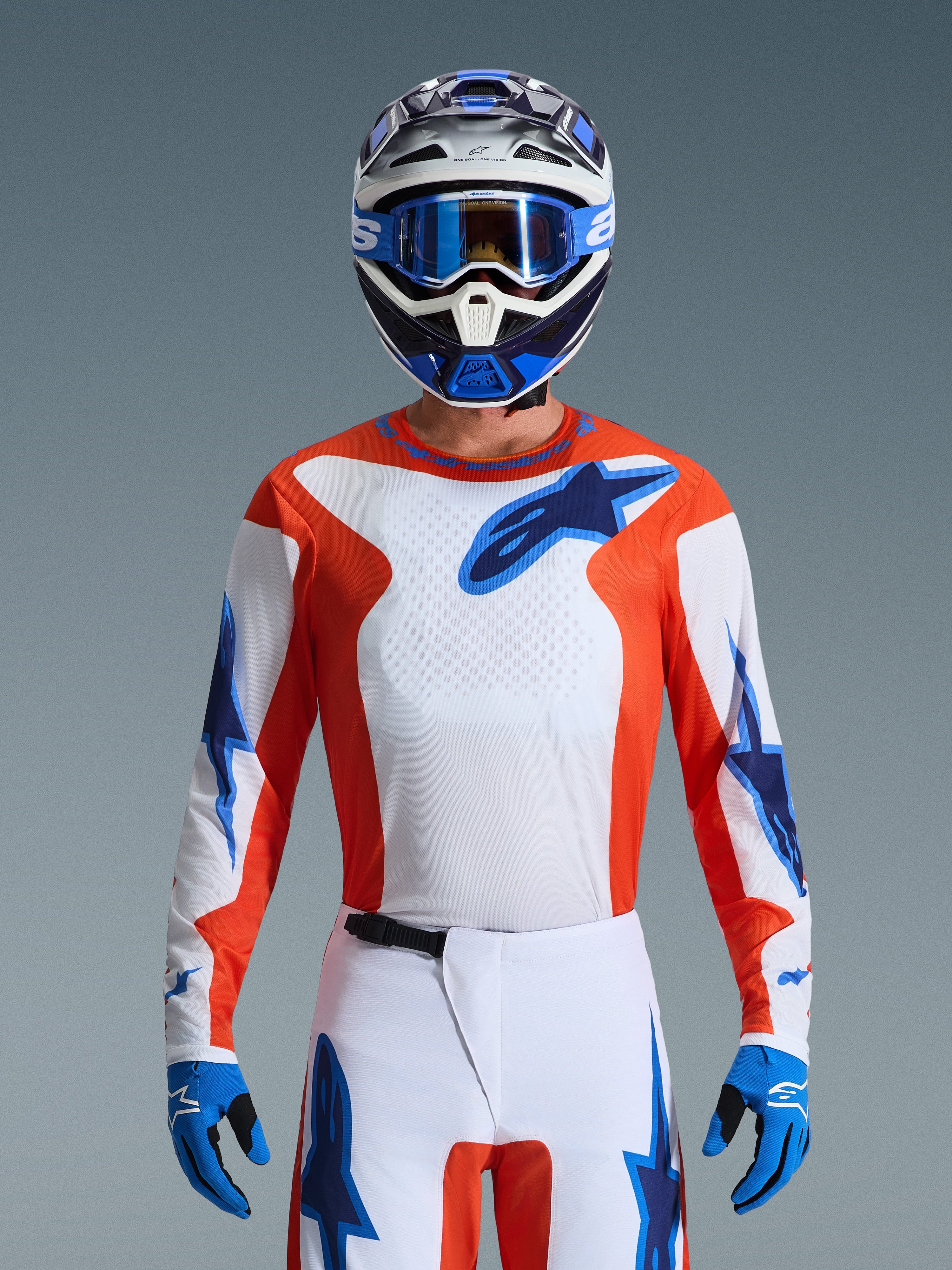 Motocross-Fahrer im 2026 Fluid Grid Jersey in Orange Ucla Blue, mit weißem Brustbereich, orangefarbenen Seitenpaneelen und blauen Alpinestars-Logos, kombiniert mit passender weiß-blauer Hose, blauen Handschuhen und einem weiß-blauen Helm für einen professionellen Offroad-Rennlook.