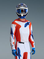 Alpinestars 2026 Fluid Grid Trikot, Motocross-Trikot in Orange UCLA Blue, getragen von einem Fahrer mit passender weiß-oranger Hose, blau-weißem Helm, blauer Brille und blauen Handschuhen, komplettes Offroad-Rennausrüstungs-Set