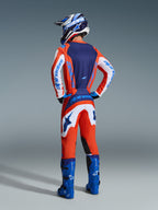 Motocross-Fahrer von hinten im Alpinestars 2026 Fluid Grid Gear Set, Trikot in Orange und UCLA-Blau mit weißen Ärmeln, passender orange-weißer Hose, blauen Motocross-Stiefeln und blau-weißem Helm, abgestimmtes Performance-Outfit für den Offroad-Rennsport