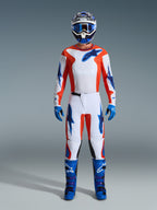 Motocross-Fahrer in kompletter Rennausrüstung, 2026 Fluid Grid Trikot in Orange und UCLA-Blau, passende weiße Hose mit orangefarbenen und blauen Akzenten, blau-weißer Helm mit blauer Schutzbrille, blau-violette Offroad-Stiefel, blaue Handschuhe, abgestimmtes Outfit für Motocross-Rennen