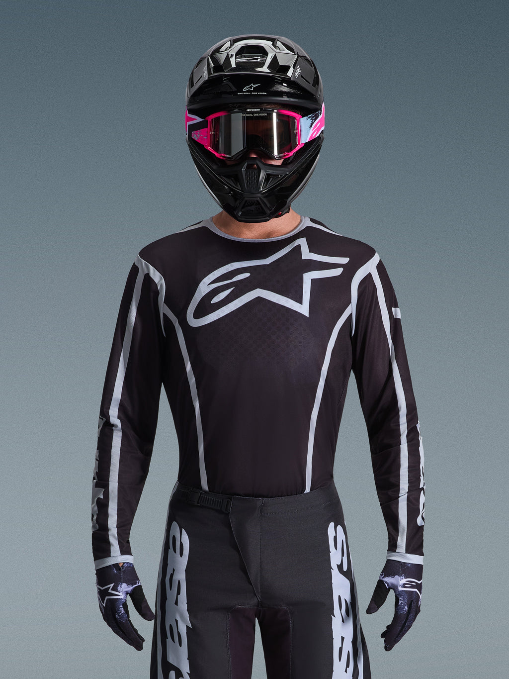 Alpinestars 2026 Fluid Apex Gear Set, Motocross jersey and pants in black and white, features large chest logo and geometric line designs, worn with a black helmet and pink goggles, performance gear for off-road motocross racing.