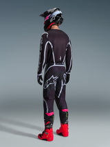 Motocross-Fahrer in kompletter Rennausrüstung, 2026 Fluid Apex Trikot in Schwarz und Grau von hinten gesehen, passende Hose mit weißen und grauen Akzenten, schwarzer Helm und leuchtend rote und pinkfarbene Stiefel, koordiniertes Outfit für Offroad-Motocross