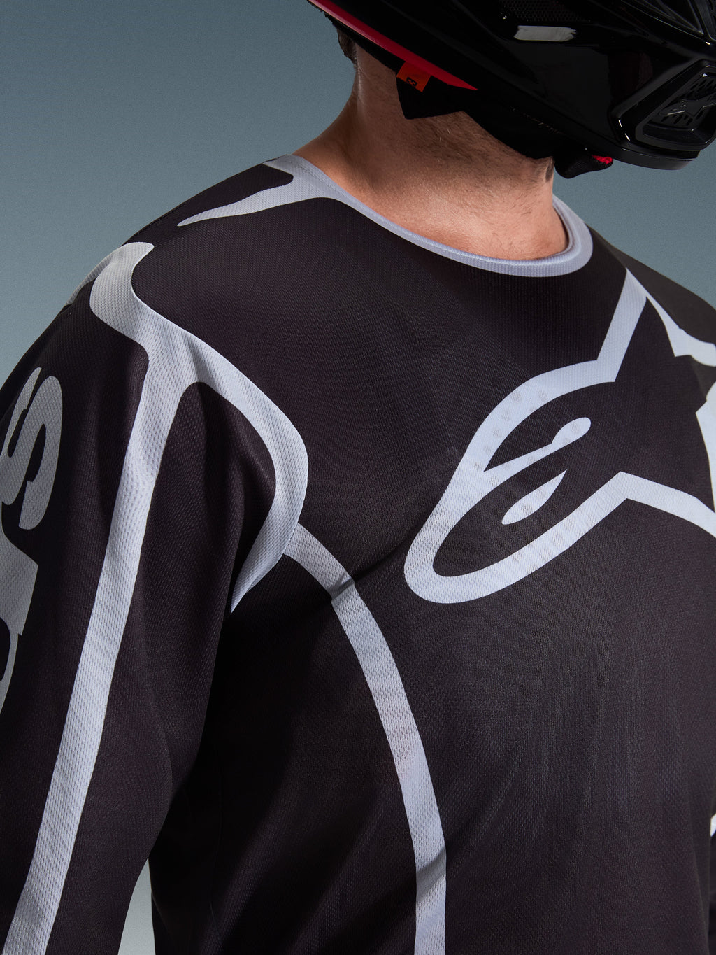 Alpinestars 2026 Fluid Apex Jersey, Motocross Jersey, Black and Grey, featuring large Alpinestars logo on the chest, sport collar, worn with a black helmet, performance gear for off-road riding