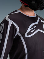 Alpinestars 2026 Fluid Apex Jersey, Motocross Jersey, Black and Grey, featuring large Alpinestars logo on the chest, sport collar, worn with a black helmet, performance gear for off-road riding