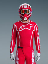Alpinestars 2026 Fluid Apex Trikot, Motocross-Trikot, Rot und Weiß, getragen von einem Fahrer mit passendem rot-weißem Helm und orangefarbener Brille, mit markantem weißem Logo auf der Brust, sportliche Passform, Teil einer abgestimmten Offroad-Rennausrüstung