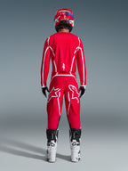 Motocross-Fahrer in der Rückansicht, Alpinestars 2026 Fluid Apex Trikot in Rot und Weiß, passende rote Hose mit markanten weißen Stern-Logos, roter Helm, weiß-schwarze Motocross-Stiefel und schwarz-weiße Handschuhe, komplette Ausrüstung für den Offroad-Rennsport