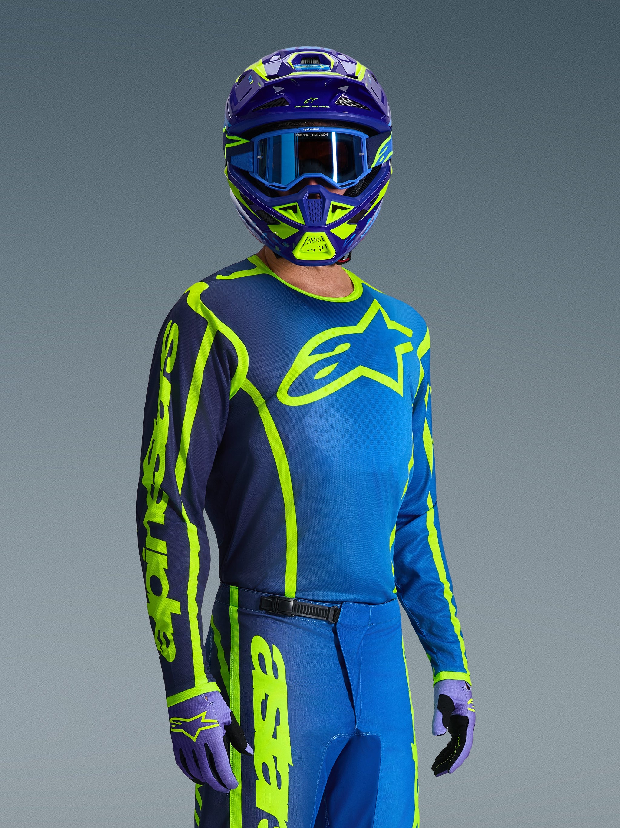 Motocross rider wearing the Alpinestars 2026 Fluid Apex Jersey in Blue and Yellow Fluo, matching blue and neon yellow pants, purple and yellow helmet with blue goggles, and coordinated gloves, complete off-road racing gear.