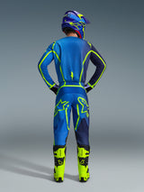 Motocross rider seen from behind in full racing gear, featuring the Alpinestars 2026 Fluid Apex Jersey and matching pants in Blue Yellow Fluo, with vibrant neon accents and bold branding, paired with bright yellow boots and a matching helmet.