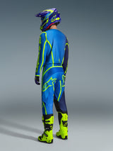 Motocross rider viewed from the back wearing the Alpinestars 2026 Fluid Apex Jersey in Blue Yellow Fluo, matching blue and fluorescent yellow pants, bright yellow boots, and a coordinated helmet, professional off-road racing gear