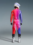 Alpinestars 2026 Fluid Apex Trikot und passende Hose, Motocross-Ausrüstungsset, mehrfarbiger rot-lila Farbverlauf, Rückansicht eines Fahrers mit weiß-schwarzen Stiefeln und weißem Helm, markante weiße Logos und geometrische Muster für den Offroad-Rennsport