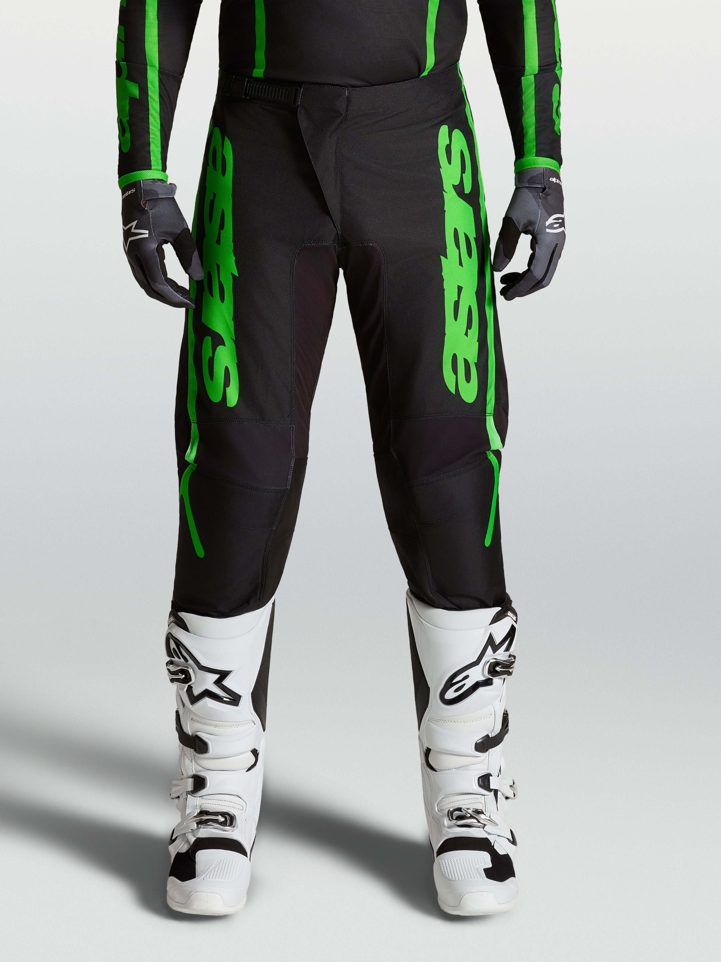 Alpinestars Fluid Apex V2 Hose, Herren Motocross-Hose in Schwarz und Grün mit verstärkten Knien und weißen Stiefeln.