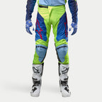 Alpinestars 2024 Racer Hoen Hose, Motocross-Hose, Gelb Fluo und Blau Night Navy, getragen mit weiß-schwarzen Motocross-Stiefeln und blauen Handschuhen, mit markanten roten Logos, hellblauen Knieeinsätzen und einem sportlichen ergonomischen Design für den Offroad-Einsatz.