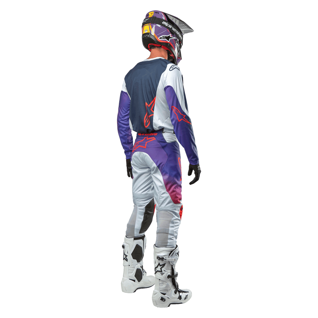 Alpinestars 2024 Racer Hoen Jersey, Motocross-Fahrer von hinten gesehen, Hellgrau, Hot Orange und Schwarz, marineblaues Rückenteil mit orangefarbenem Stern-Logo, lila Ärmel, kombiniert mit passender Rennhose und weißen Stiefeln.