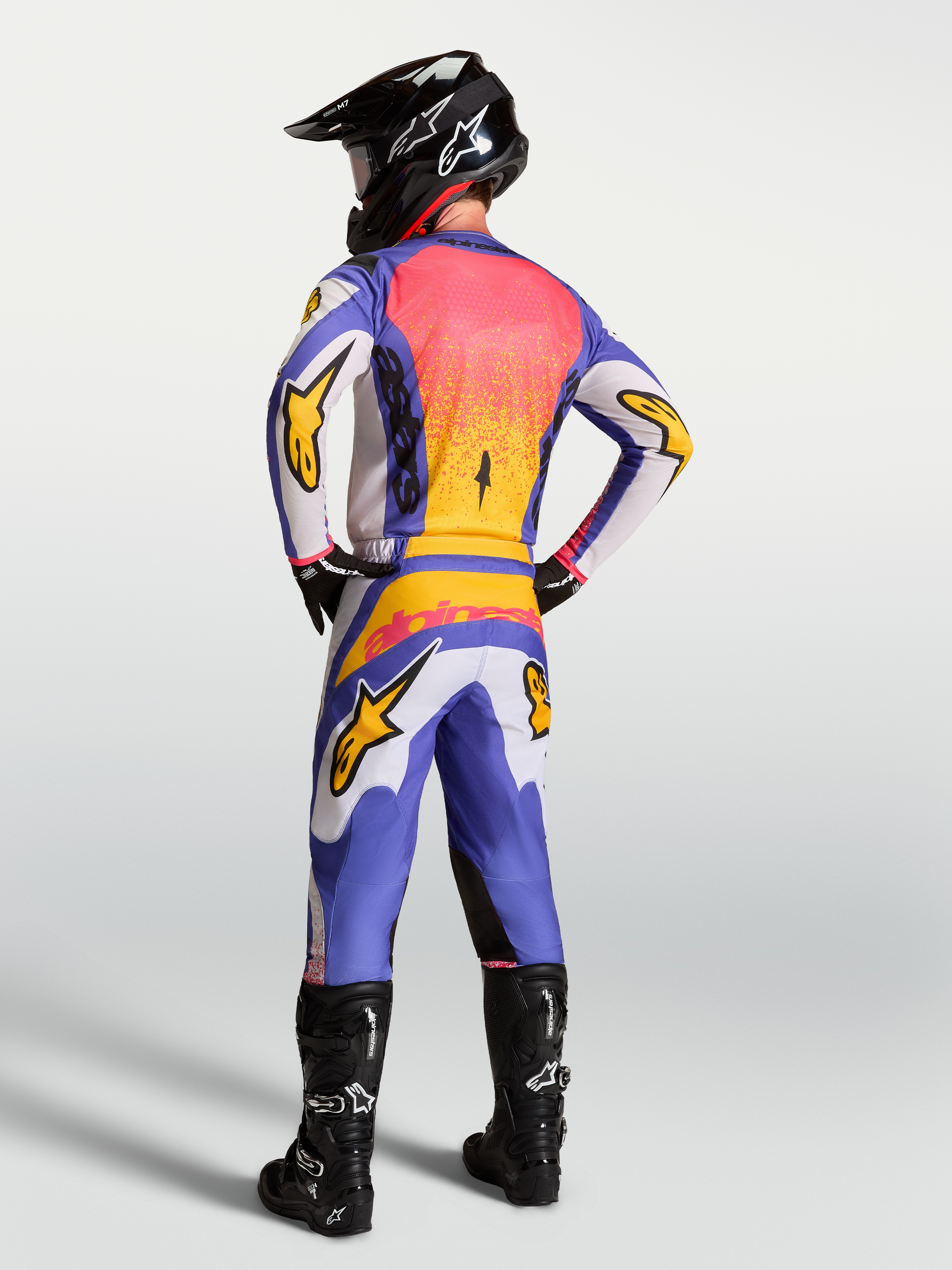 Alpinestars Fluid Drag Trikot in Lila und Blau mit Gold, Rückansicht eines Motocross-Fahrers in voller MX-Ausrüstung.