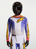 Alpinestars Fluid Drag Trikot, Motocross-Trikot für Herren in Blau Iris und Gold, feuchtigkeitsableitendes Gewebe, sportlicher Schnitt, getragen mit MX-Helm und Schutzbrille.