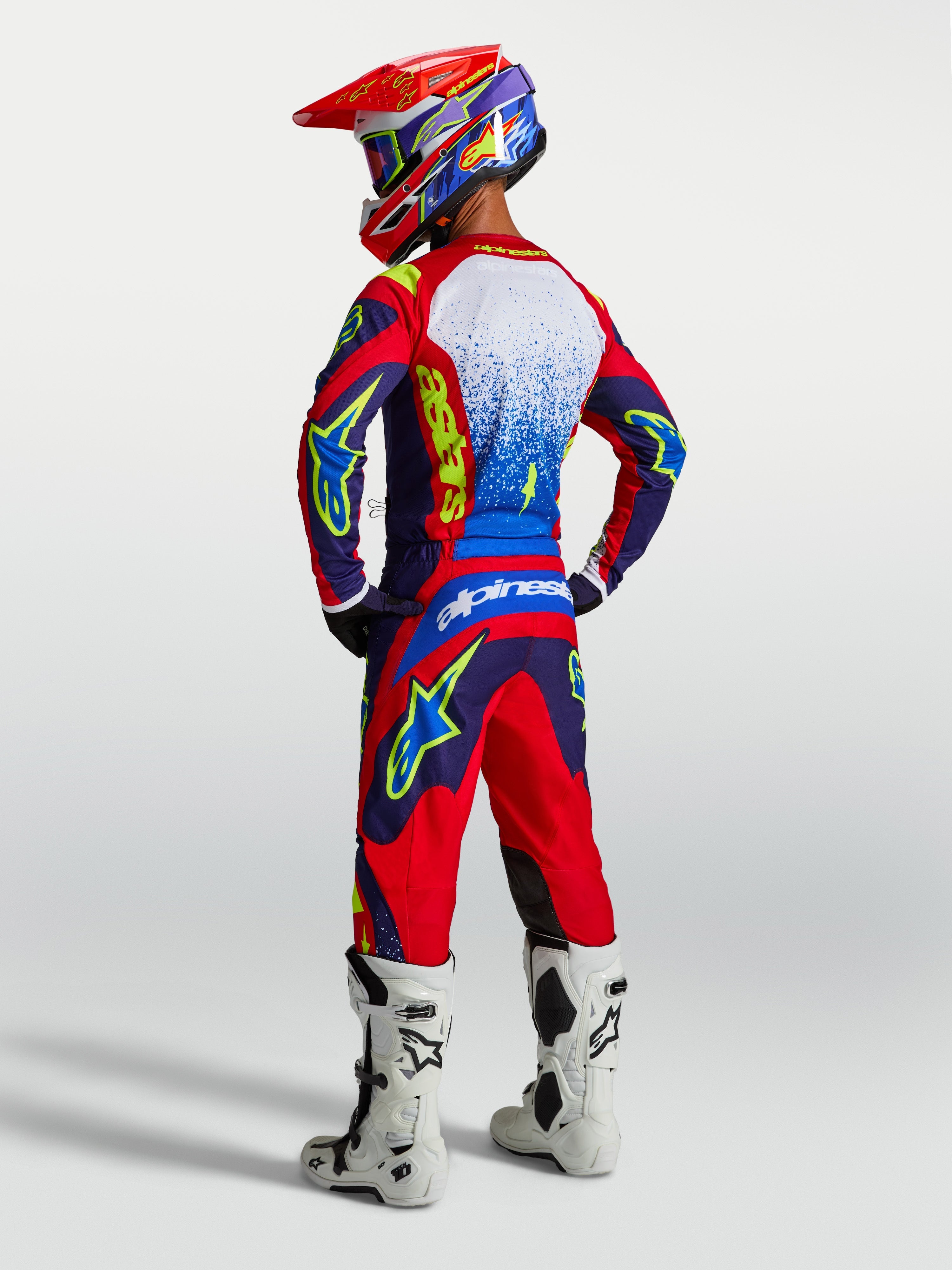 Alpinestars Fluid Drag Trikot, Herren-Motocross-Oberteil, Blau und Rot, Rückansicht mit passender Ausrüstung und weißen Stiefeln.