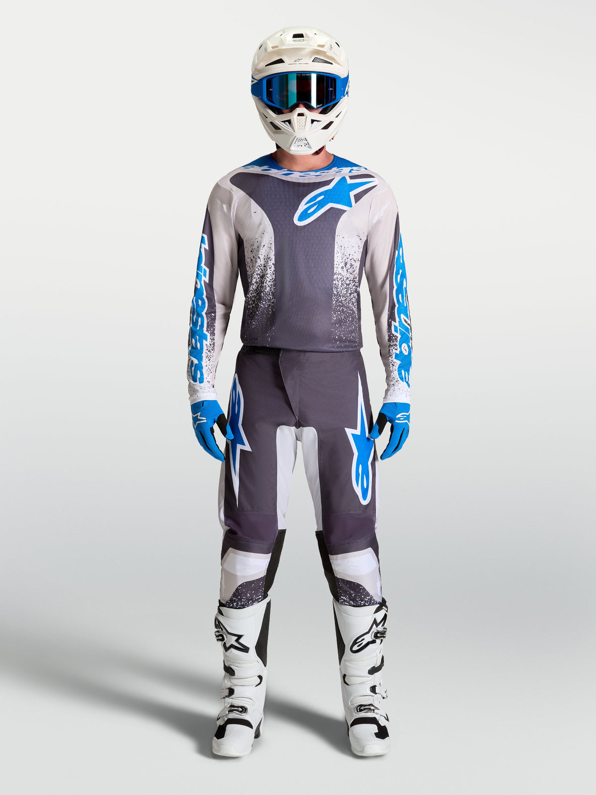 Alpinestars Fluid Drag Ausrüstungsset, Motocross-Trikot und Hose in Grau und Blau, getragen mit Helm und Stiefeln, für professionelle Offroad-Performance.