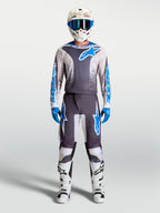Alpinestars Fluid Drag Trikot in Grau und Blau, atmungsaktives MX-Trikot mit weißem Helm und Motorradstiefeln.