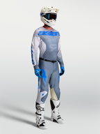 Alpinestars Racer Amber Trikot, aschgraue und UCLA-blaue Motocross-Ausrüstung für Herren am Model mit Helm und Stiefeln.