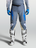 Alpinestars Racer Amber Hose 2027, Herren Motocross-Hose in Aschgrau und Blau, getragen mit weißen Rennstiefeln.