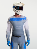 Alpinestars Racer Amber Trikot, Motocross-Ausrüstung für Herren, Grau und UCLA Blau, mit weißem MX-Helm und Schutzbrille.