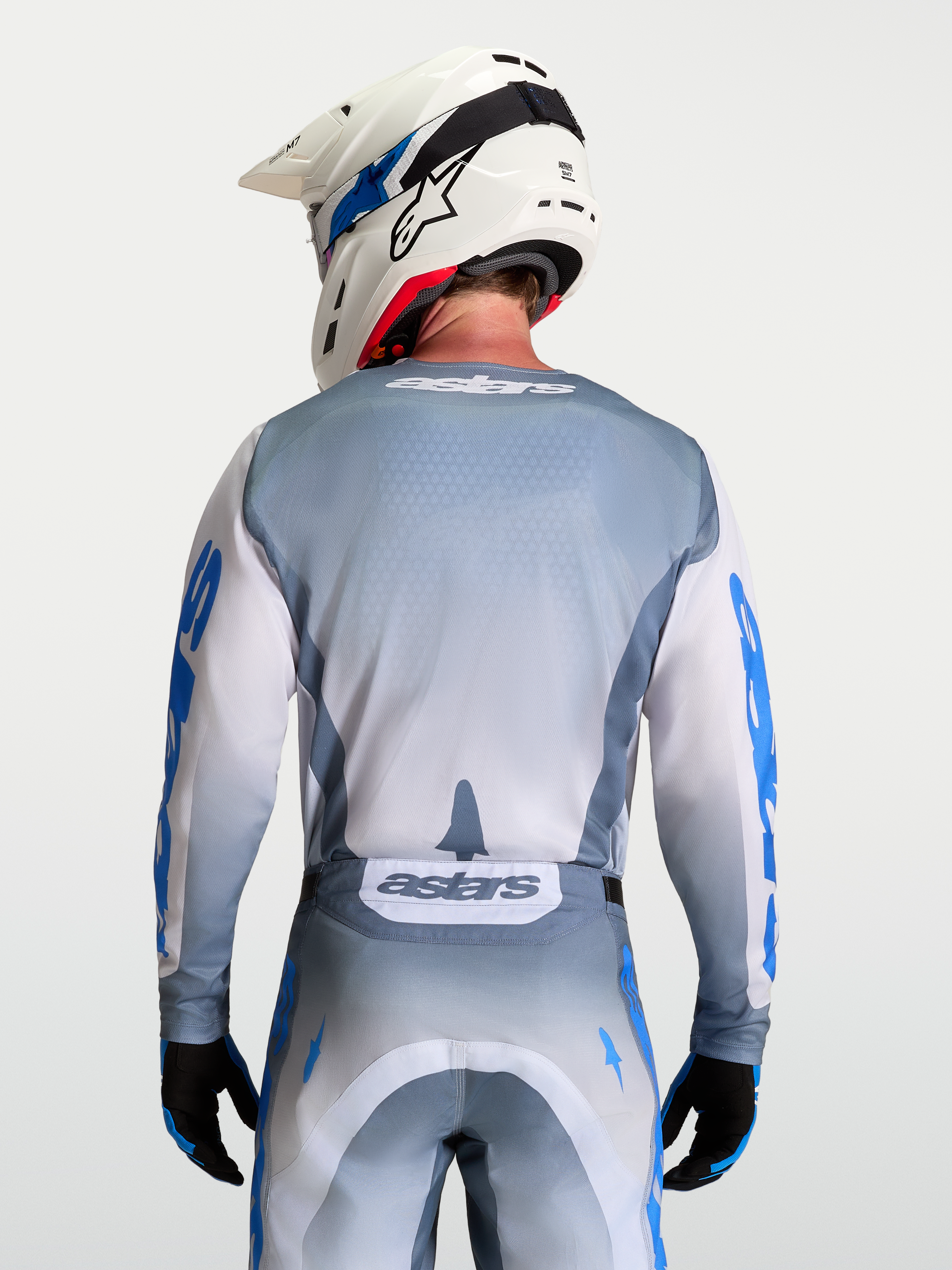 Alpinestars Racer Amber Trikot, Motocross-Trikot in Aschgrau und Weiß, rückseitige Modellansicht mit weißem Helm, ergonomische Passform für Offroad-Rennen