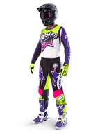 Motocross rider wearing Alpinestars Limited Edition Supertech Dirt Studios® gear, White Purple and Yellow Fluo color scheme, black pants with bold purple and pink star logos, neon yellow gloves, purple and white racing boots, black helmet, complete professional racing kit for off-road performance
