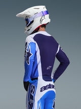 Motocross-Fahrer im Alpinestars 2026 Racer Air Portl Trikot in Ucla Blue und Weiß, Rückansicht mit Fokus auf das atmungsaktive marineblaue Mesh-Rückenteil, kombiniert mit passender Hose, weißem Alpinestars-Helm und blauer Brille, abgestimmtes Motocross-Ausrüstungsset.