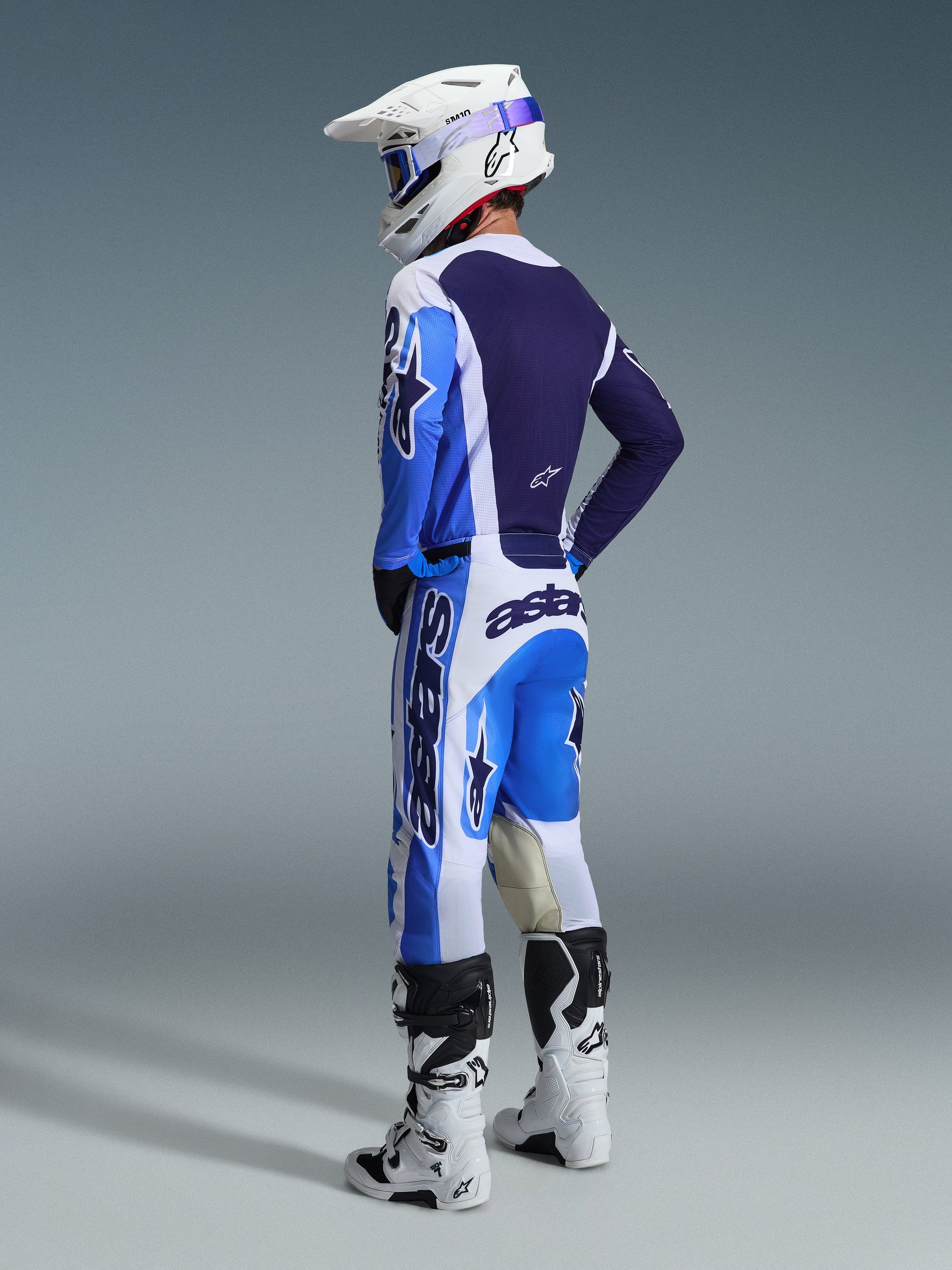 Motocross-Fahrer in der Rückansicht im Alpinestars 2026 Racer Air Portl Trikot in Ucla Blau und Weiß, kombiniert mit passender Motocross-Hose, weißem Supertech Helm und weißen Stiefeln, zeigt ein komplettes, koordiniertes Rennsport-Ausrüstungsset.