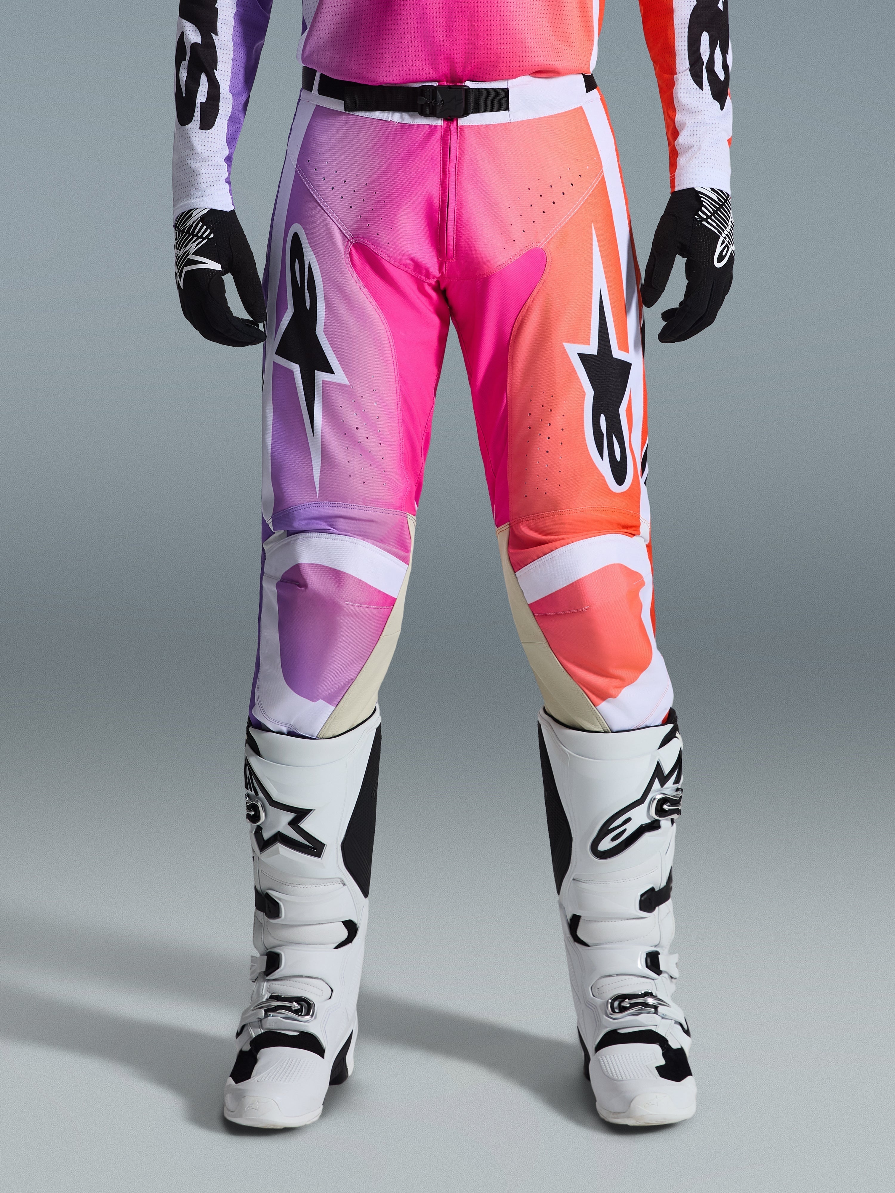 Alpinestars 2026 Racer Air Portl Hose, Motocross-Hose, lebhafter Farbverlauf in Lila, Pink und Orange, mit markanten Stern-Logos auf den Oberschenkeln, getragen mit weißen Rennstiefeln und schwarzen Handschuhen, entwickelt für High-Performance-Offroad-Fahrten.