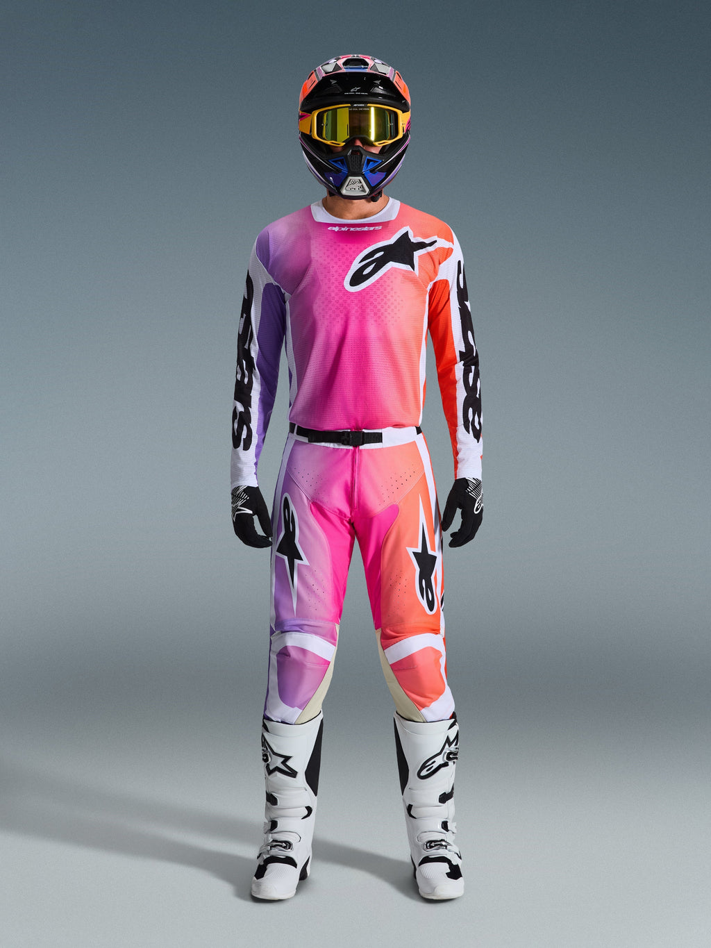Motocross rider wearing full Alpinestars 2026 Racer Air Portl racing gear, featuring a pink, purple, and orange gradient design on the pants and jersey, paired with a matching helmet, yellow goggles, white boots, and black gloves for a coordinated off-road look.