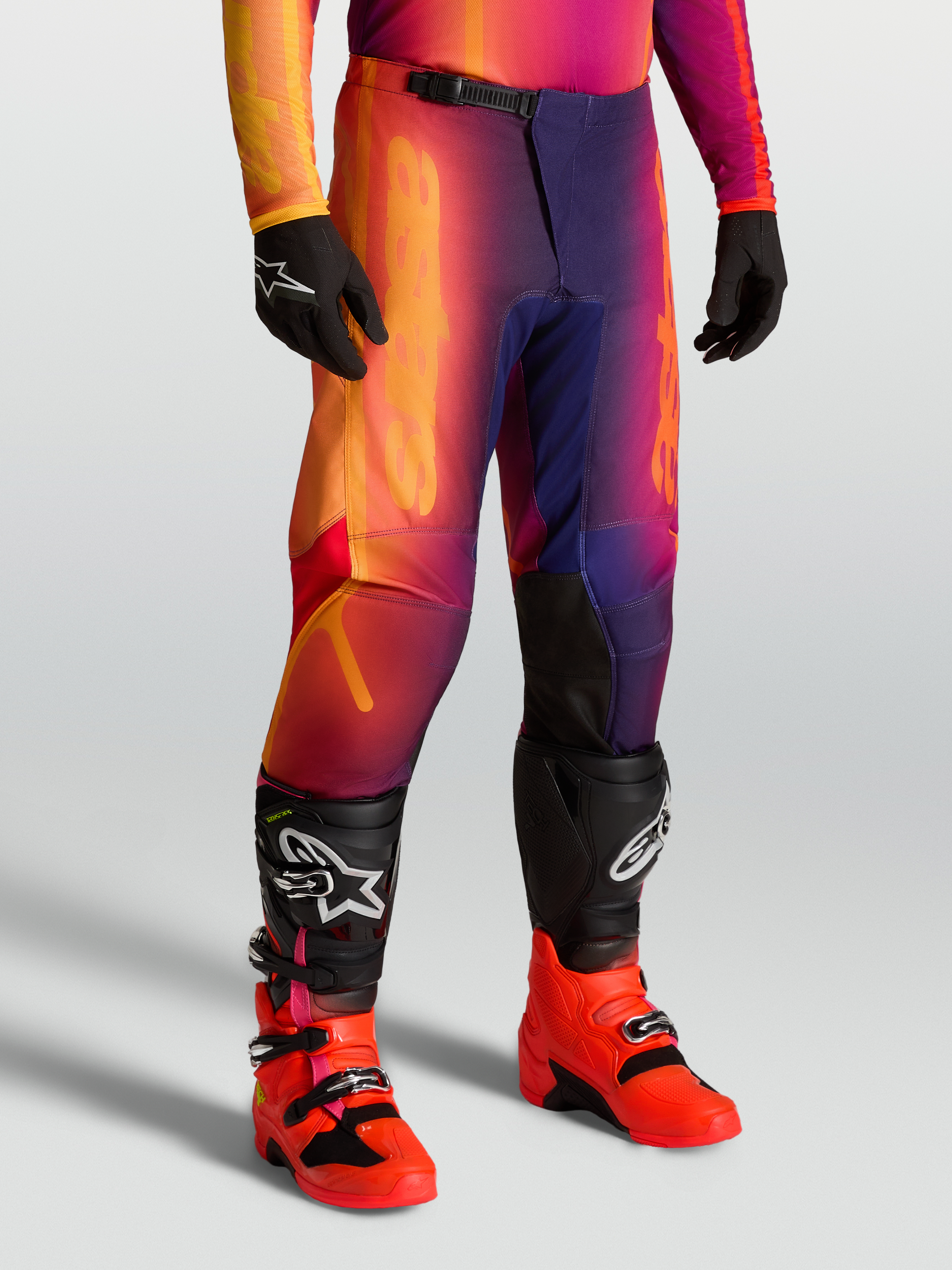 Alpinestars Fluid Kepler Hose, Offroad-Motocross-Hose in Lila und Orange, sportliche Passform, getragen mit Tech-Stiefeln und Handschuhen.