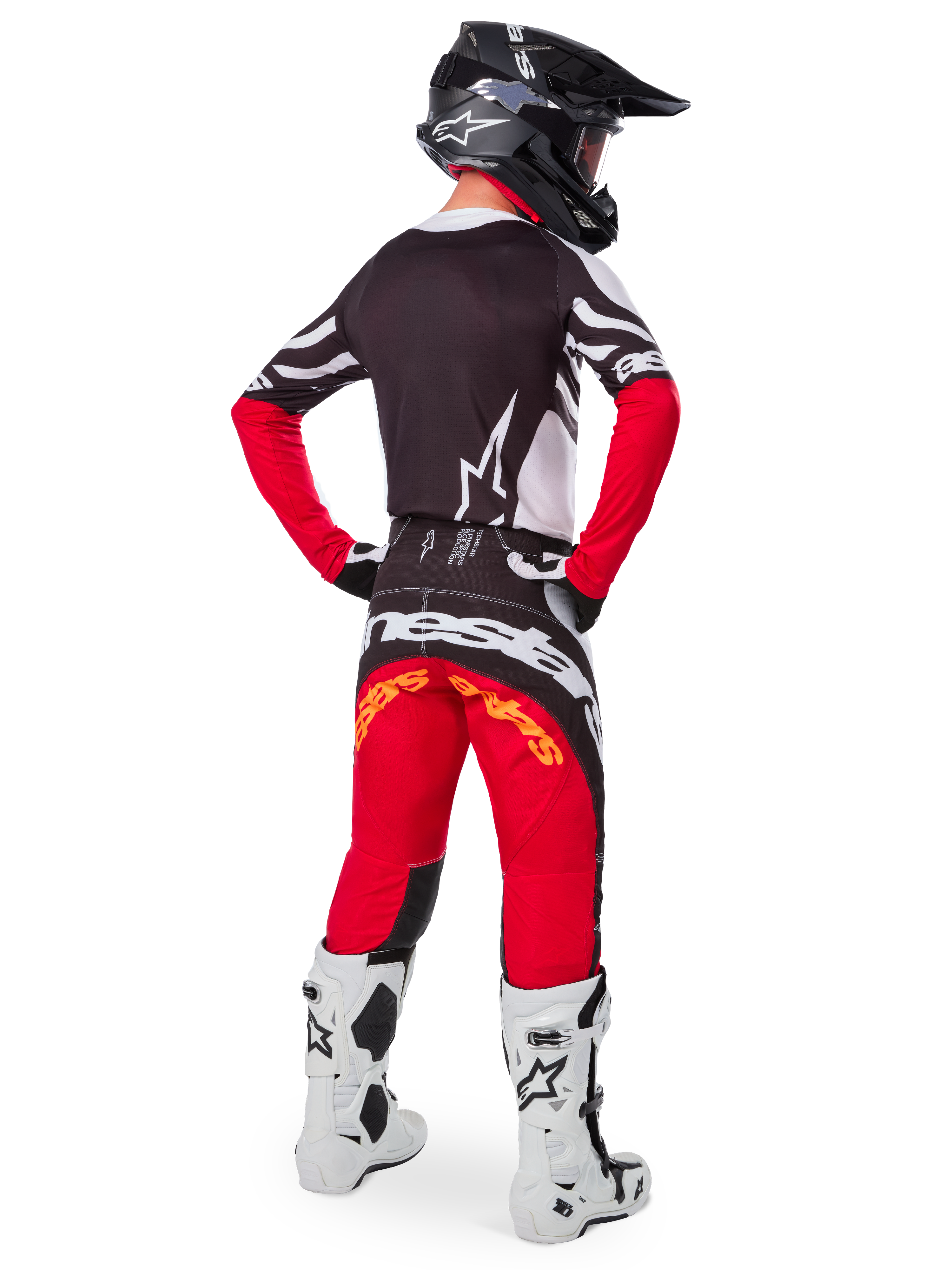 Alpinestars Limited Edition Techstar Deep Gear Set, Rückansicht eines Motocross-Fahrers, schwarzes Trikot mit weißen und roten Akzenten, passende rot-schwarze Hose mit Alpinestars-Branding, weiße Rennstiefel und schwarzer Helm, komplette Offroad-Rennausrüstung